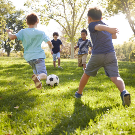 Four schoolboys playing soccer in the park