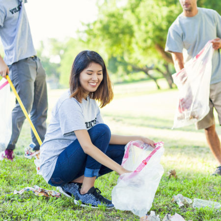 Group of diverse millennials volunteering in local park by picking up garbage