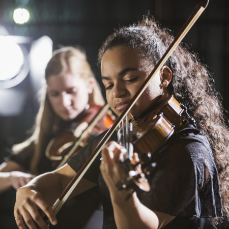 Two teenage girls playing the violin on stage